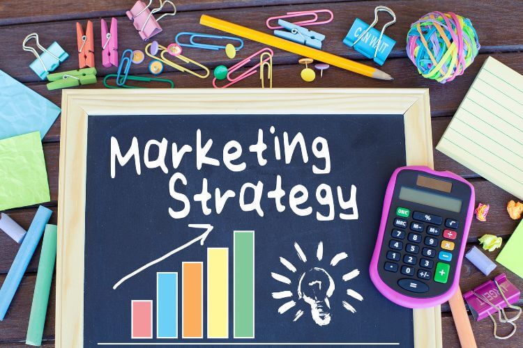 A chalkboard displays Marketing Strategy with a growth chart, calculator on it.
