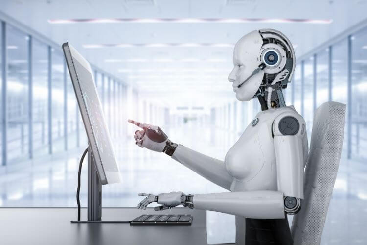 A humanoid robot with a sleek design types on a computer in a bright, futuristic office. 
