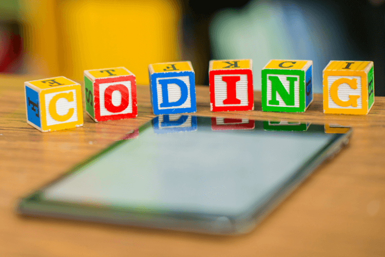 Colorful alphabet blocks spelling ‘CODING’ placed on tablet, representing simplified view of vibe coding