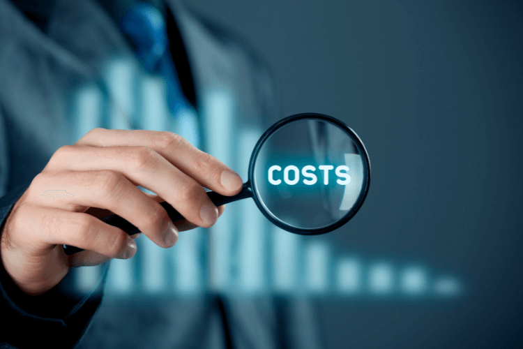 Businessman holding magnifying glass labeled “COSTS” against a blurred bar graph background comparing database efficiency