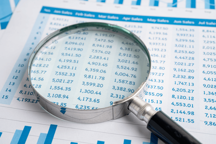 Magnifying glass focusing on financial spreadsheet numbers for data analysis.